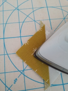 Use the point of the iron to slowly fold the darker half flat over the seam allowance, starting in the center, then pushing forward to cover the whole square.